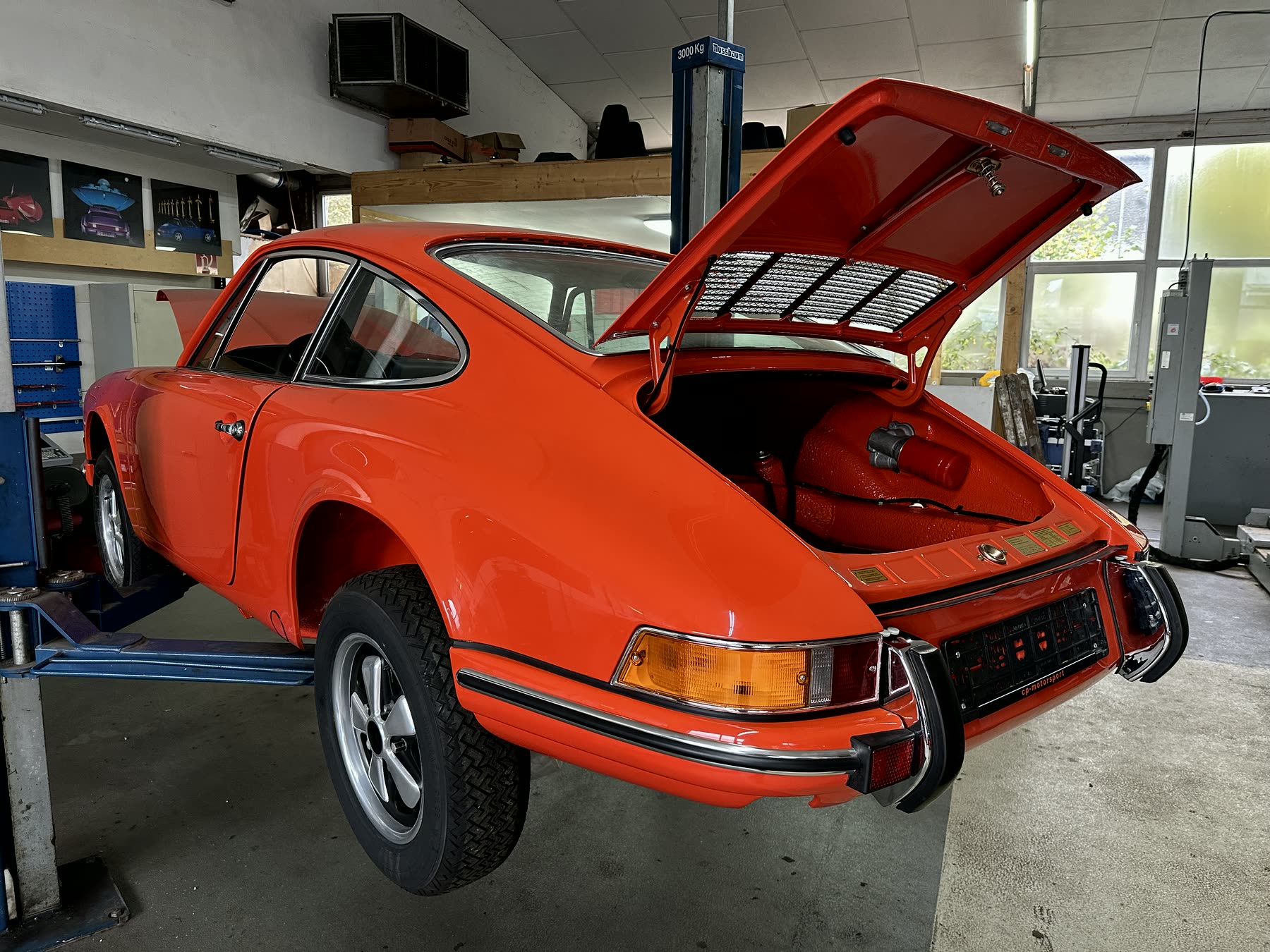 Fertig restaurierter orangeroter Porsche 911 mit geöffneter Fronthaube in der Halle